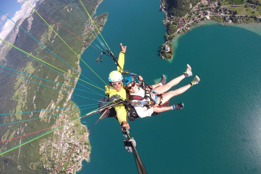 Deux personnes souriantes en plein vol en parapente, profitant de la vue et de la sensation de liberté dans les airs.