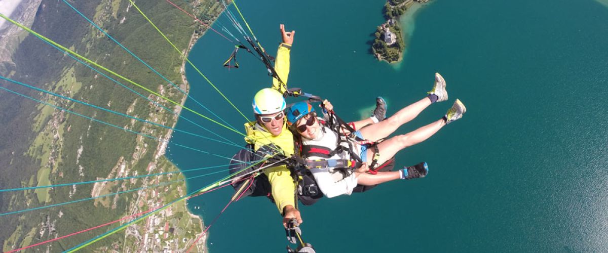 Deux personnes souriantes en plein vol en parapente, profitant de la vue et de la sensation de liberté dans les airs.