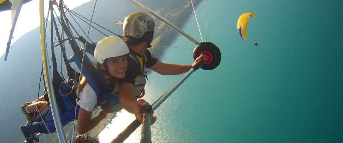 Deltaplane avec des personnes souriantes survolant le lac d'Annecy, offrant une vue panoramique sur l'eau et les montagnes environnantes