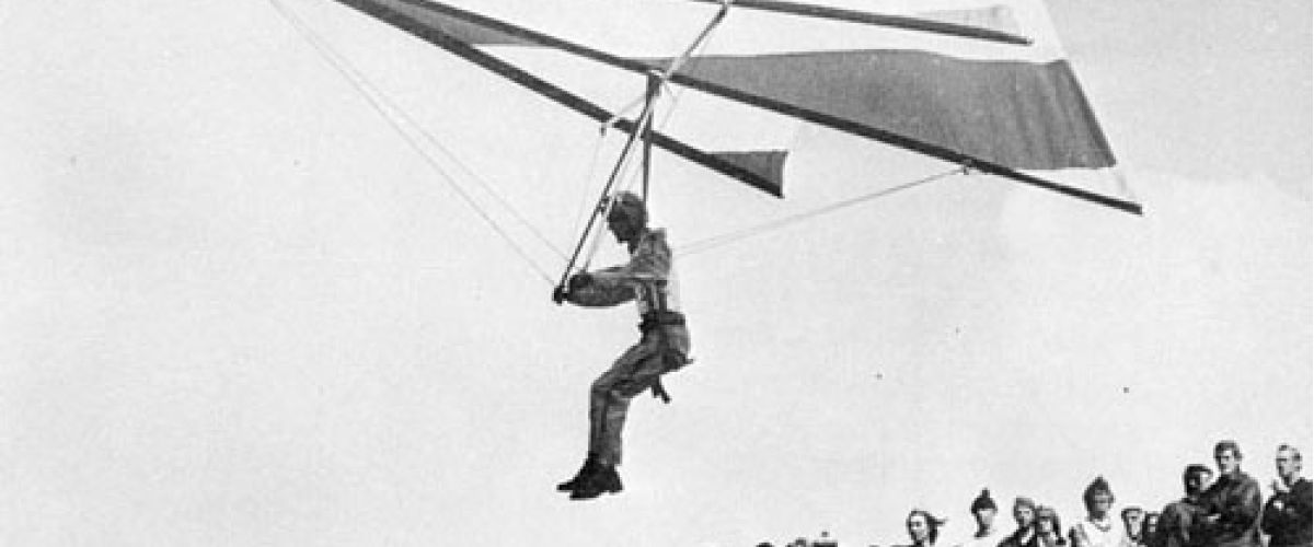 Ancienne photo montrant un deltaplane des débuts avec du public admirant le vol