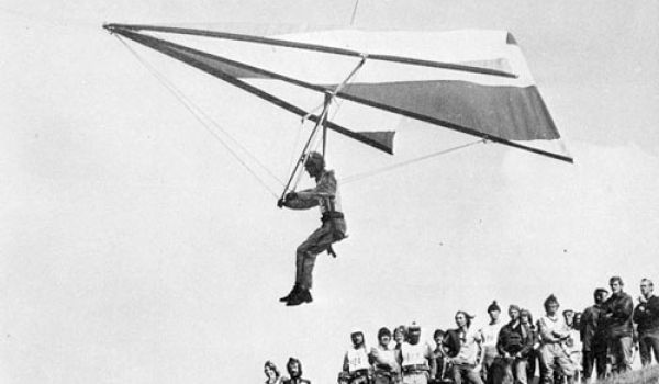 Ancienne photo montrant un deltaplane des débuts avec du public admirant le vol