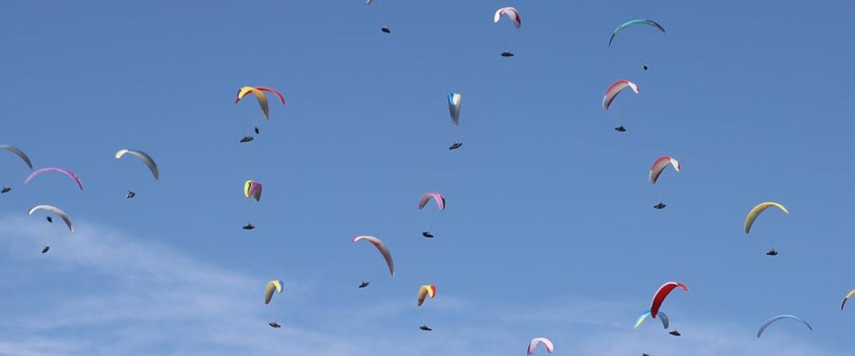 Ciel bleu clair rempli de parapentes colorés en vol